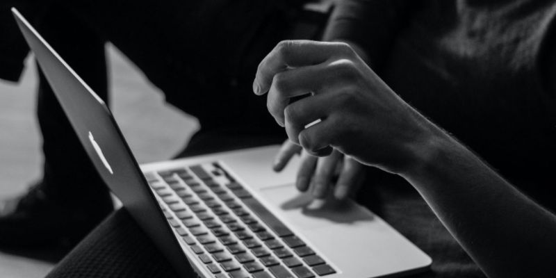 A black and white photo of a person’s hands operating a laptop; JackpotCity Casino Blog