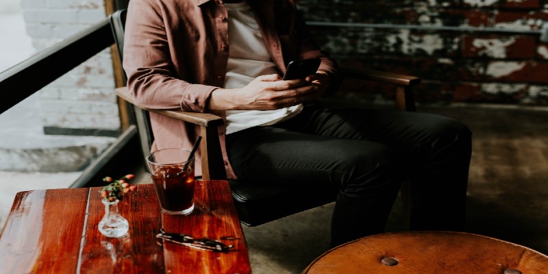 A man sitting in a café plays on his smartphone.