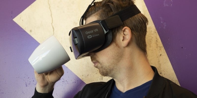 Un homme regarde une tasse via le casque de réalité virtuelle qu’il porte - Spin Palace Blogue
