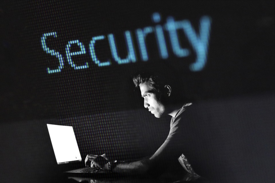 A hacker works on a computer as the word “Security” hangs above him.