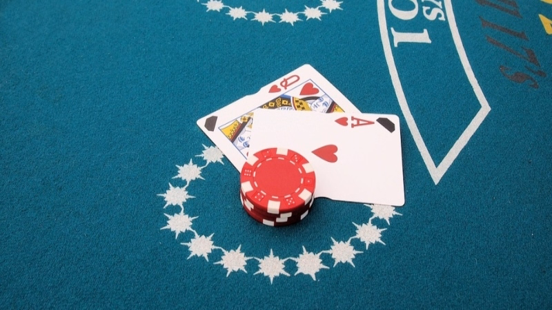 Blackjack table with an Ace of hearts and Queen of spades next to a red casino chip, representing a winning hand of 21.
